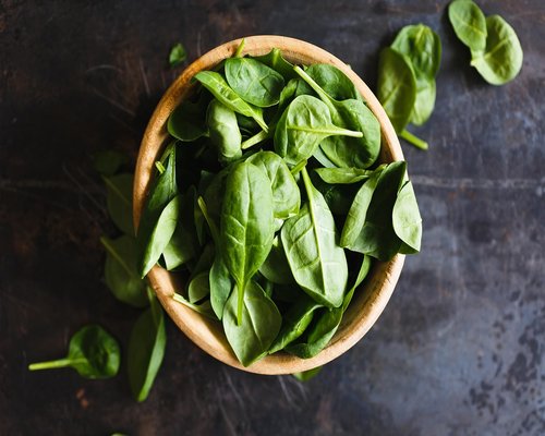 Fresh bunch of vibrant green spinach, kale, and bok choy leaves on a wooden cutting board.