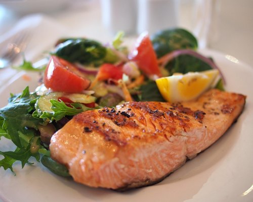 A grilled salmon fillet seasoned with herbs and lemon slices placed on a white plate with asparagus.